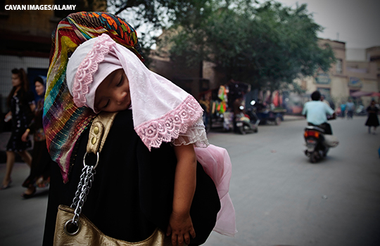 A young Uyghur girl sleeping on her mother's arm on a street in Kashgar, Xinjiang, China